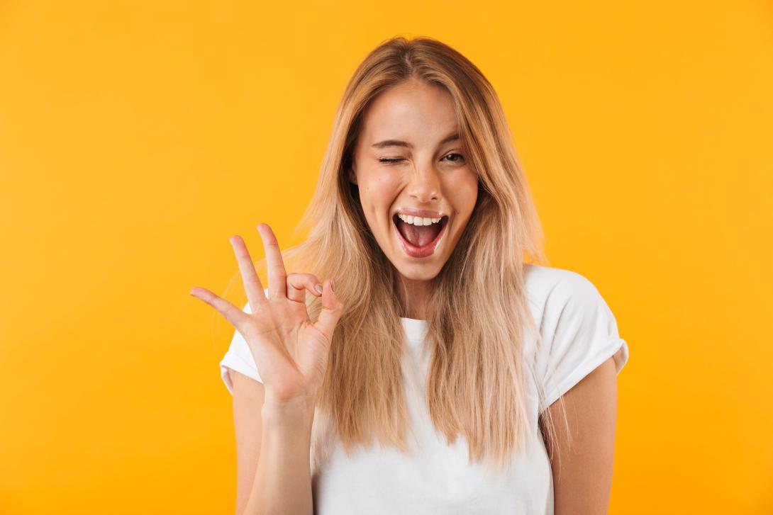 Femme souriante qui fait un clin d'œil et montre que tout va bien de la main droite